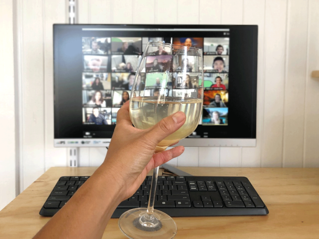 Holding a glass of white wine up during a virtual chat for virtual happy hour